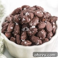 Glossy chocolate covered almonds with sea salt in a white bowl.