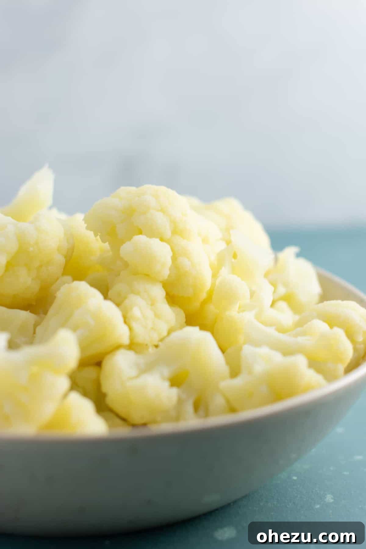 Freshly steamed cauliflower florets in a white bowl, ready to be seasoned