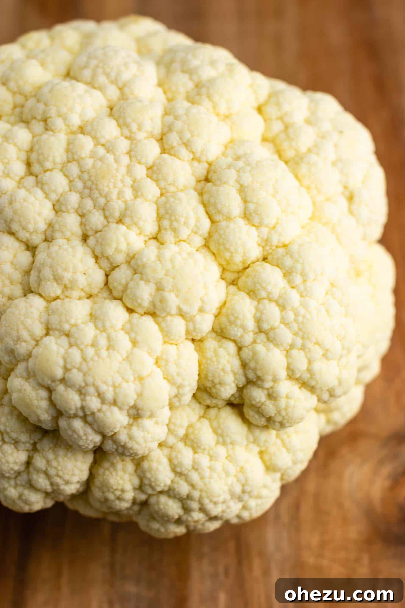 A whole head of fresh, white raw cauliflower on a cutting board