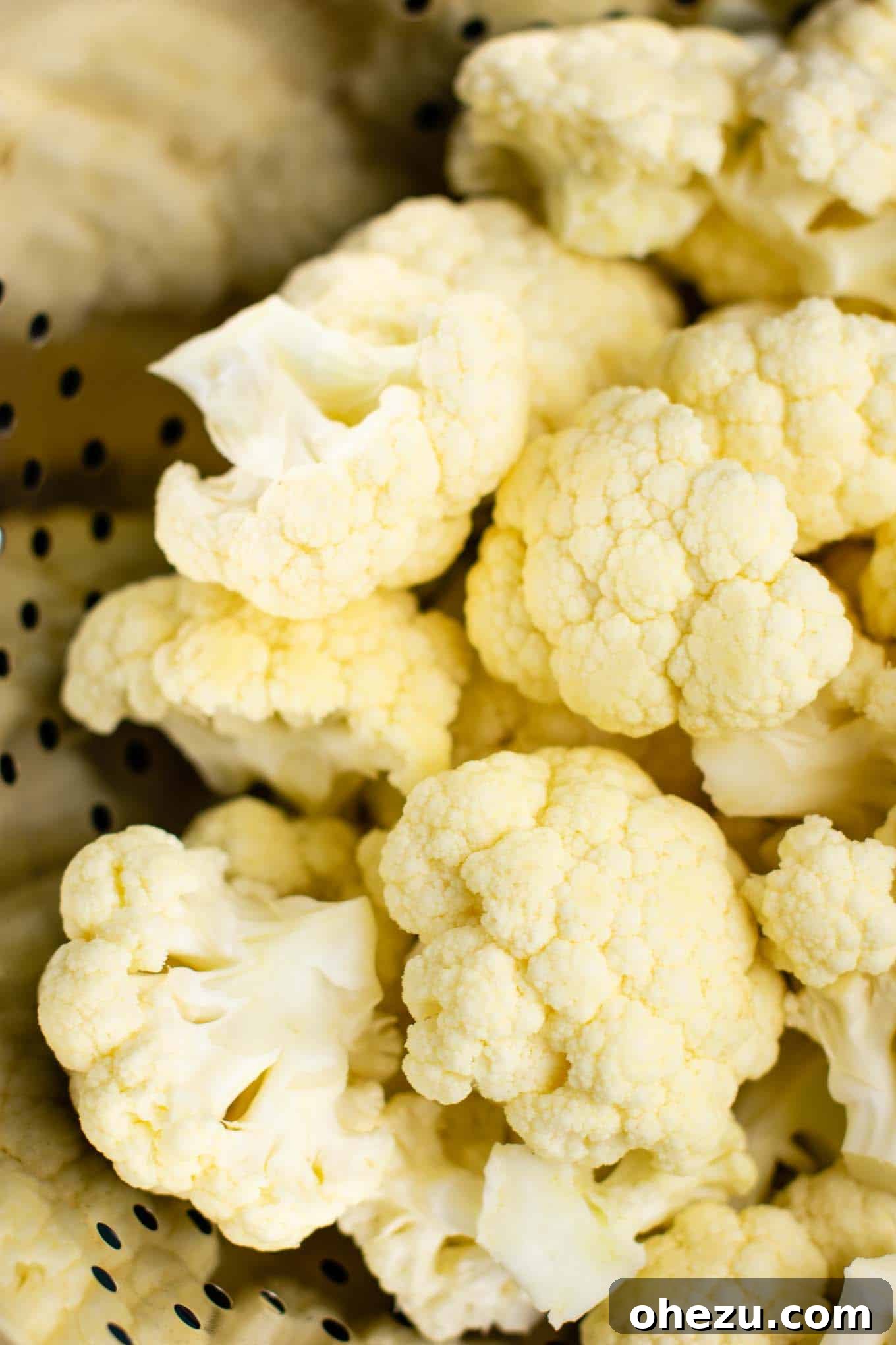 Clean, uniform cauliflower florets placed in a metal colander, ready for steaming