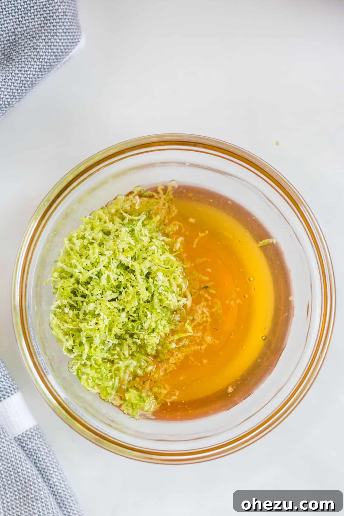 A small glass bowl containing golden honey and vibrant green lime zest, perfectly prepared and ready to be mixed into the dressing for the fruit salad.