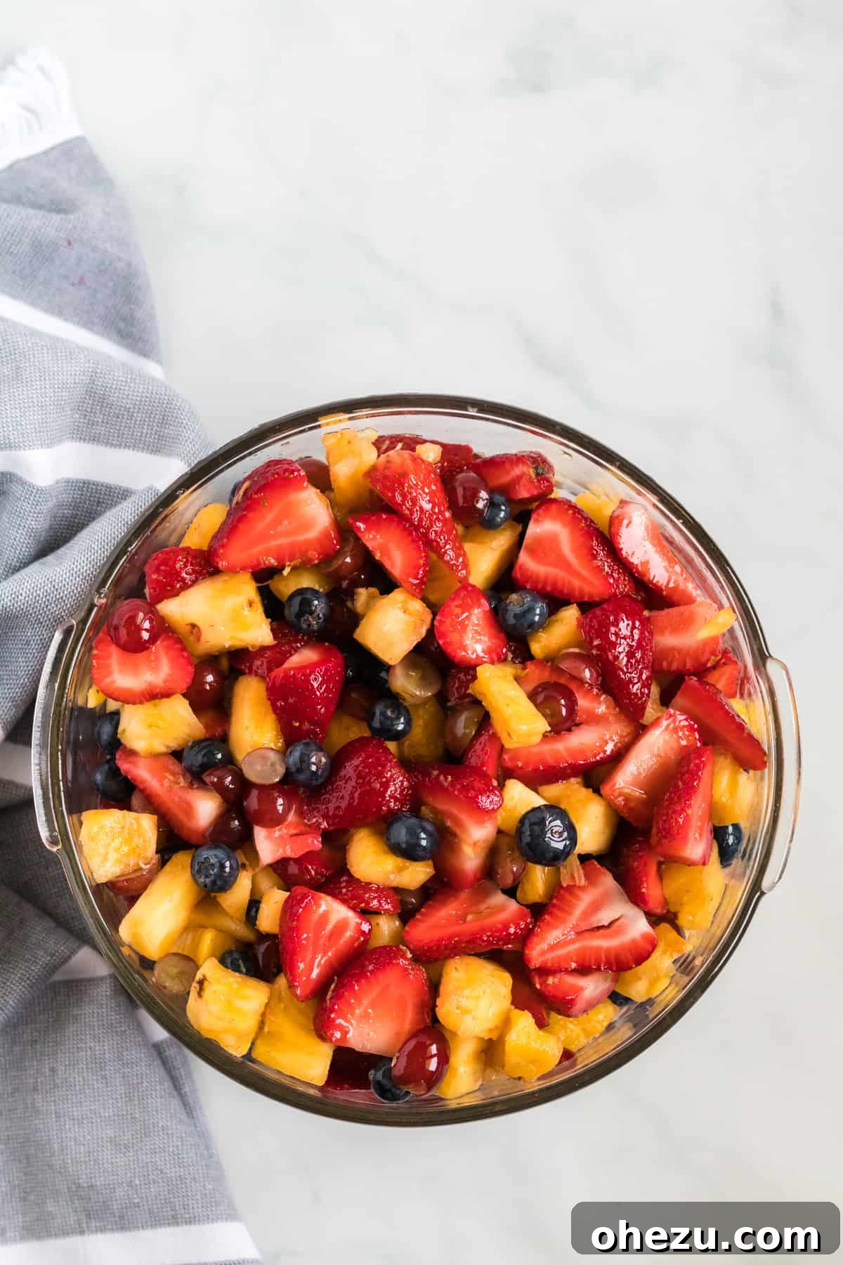 A beautifully arranged simple fruit salad with honey-lime dressing in a large glass bowl, ready to be served, showcasing the vibrant colors of fresh berries, pineapple, and grapes glistening with dressing.