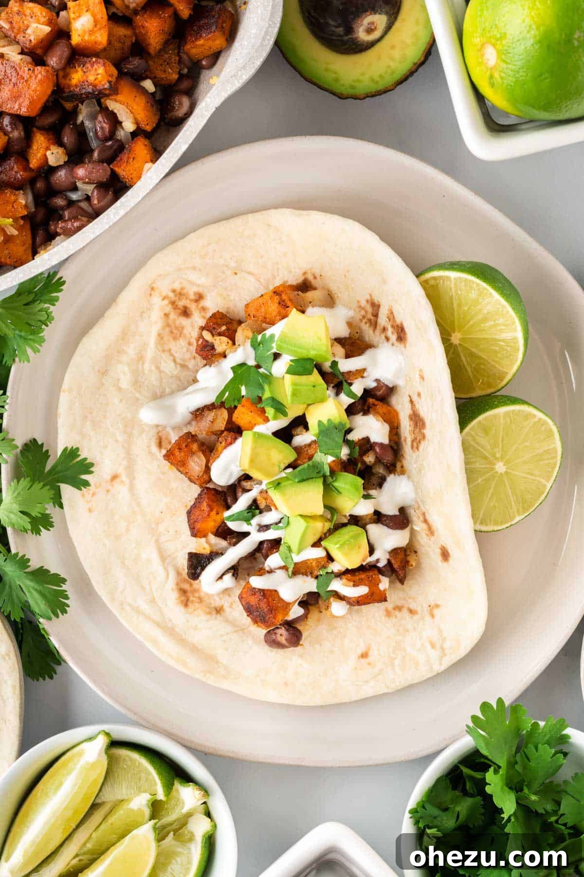 An open-faced black bean sweet potato taco on a plate, generously topped with sour cream, cilantro, and avocado