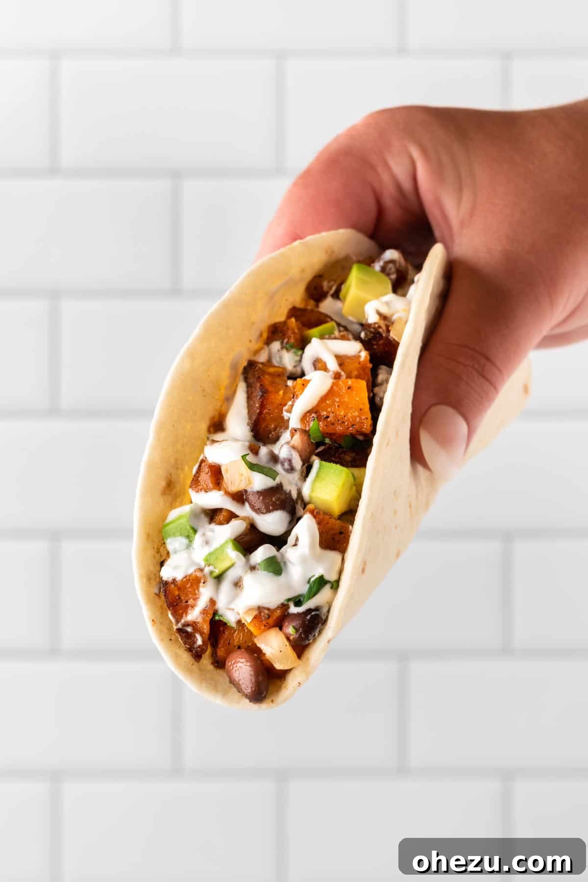 A hand holding a beautifully assembled sweet potato soft taco, ready to be eaten
