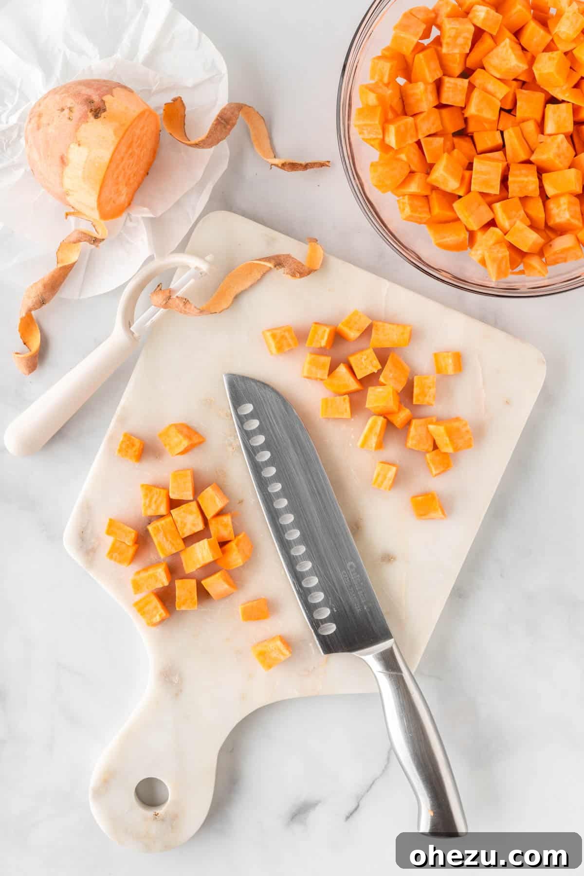 Chef dicing sweet potatoes into small, even chunks on a cutting board