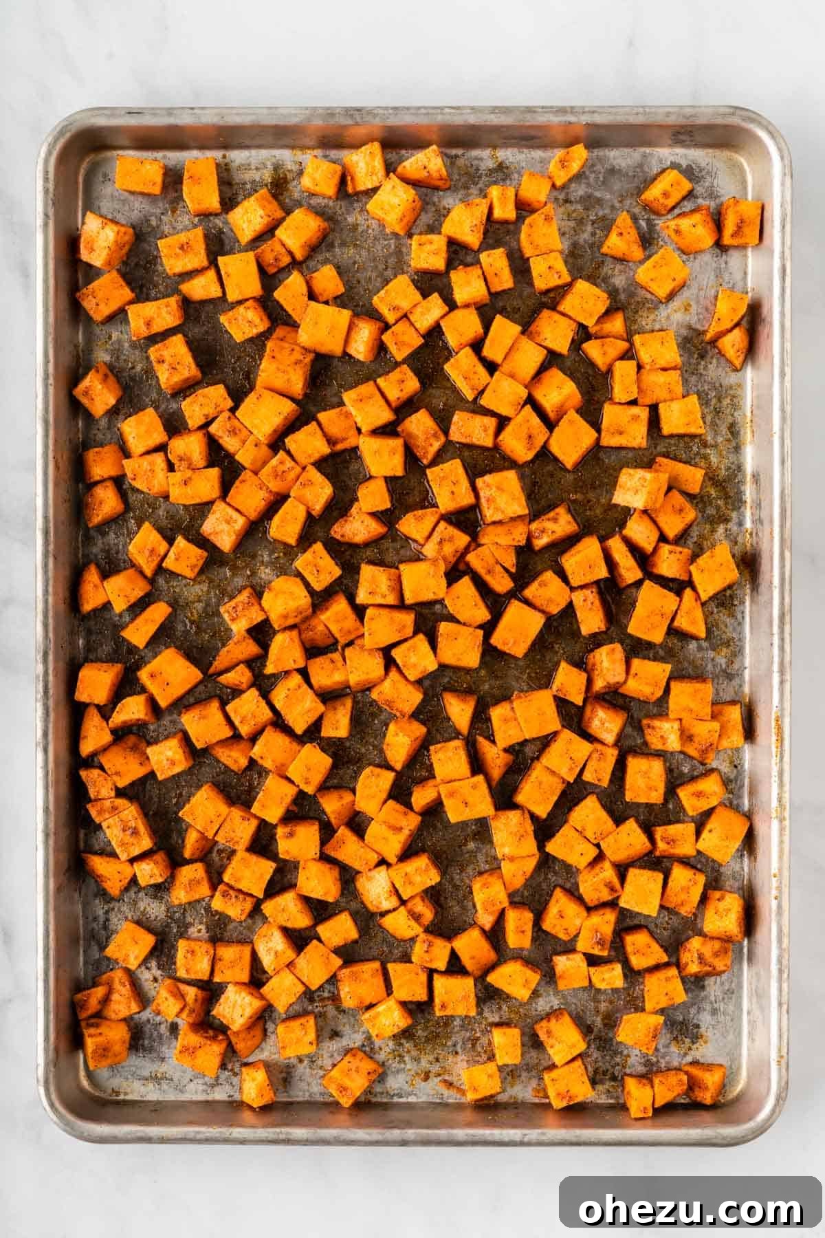 Seasoned sweet potatoes spread evenly on a baking sheet, ready for the oven