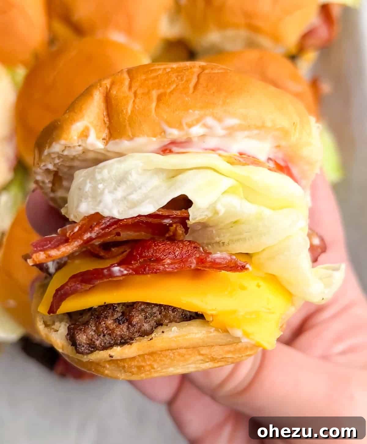 Close-up of a stack of Jr. Bacon Cheeseburger Sliders, showcasing melted cheese, crispy bacon, and fresh ingredients.