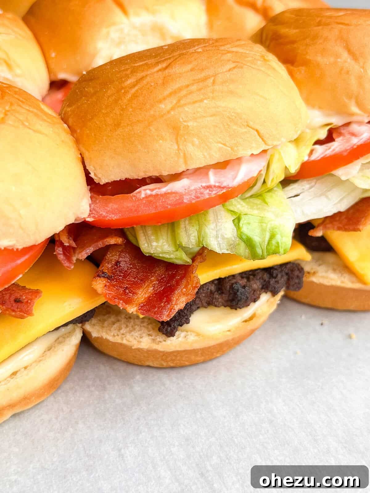 A close-up shot of a single Jr. Bacon Cheeseburger Slider, showcasing the layers of meat, cheese, bacon, lettuce, tomato, and mayo.