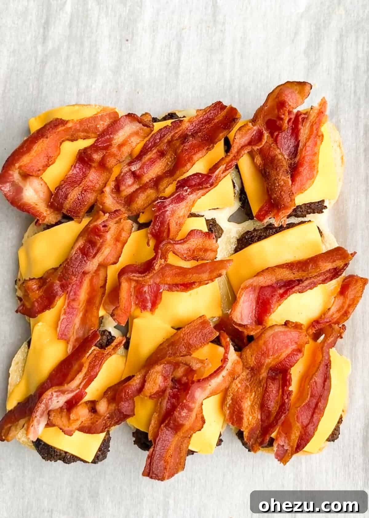 Process shot: Assembling Jr. Bacon Cheeseburger Sliders with mayo, patty, cheese, and vegetables.