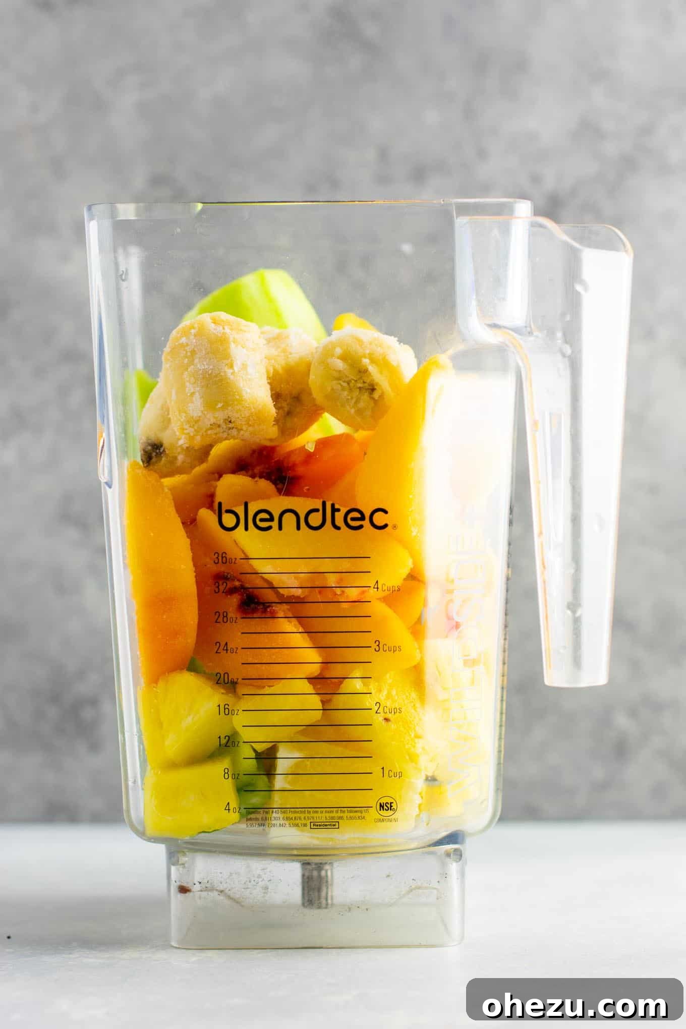 Sunshine Detox Blend 4 All the fresh ingredients for the pineapple detox smoothie laid out: pineapple chunks, cucumber, celery stalks, lemon, ginger root, frozen banana slices, frozen peaches, and ice cubes.