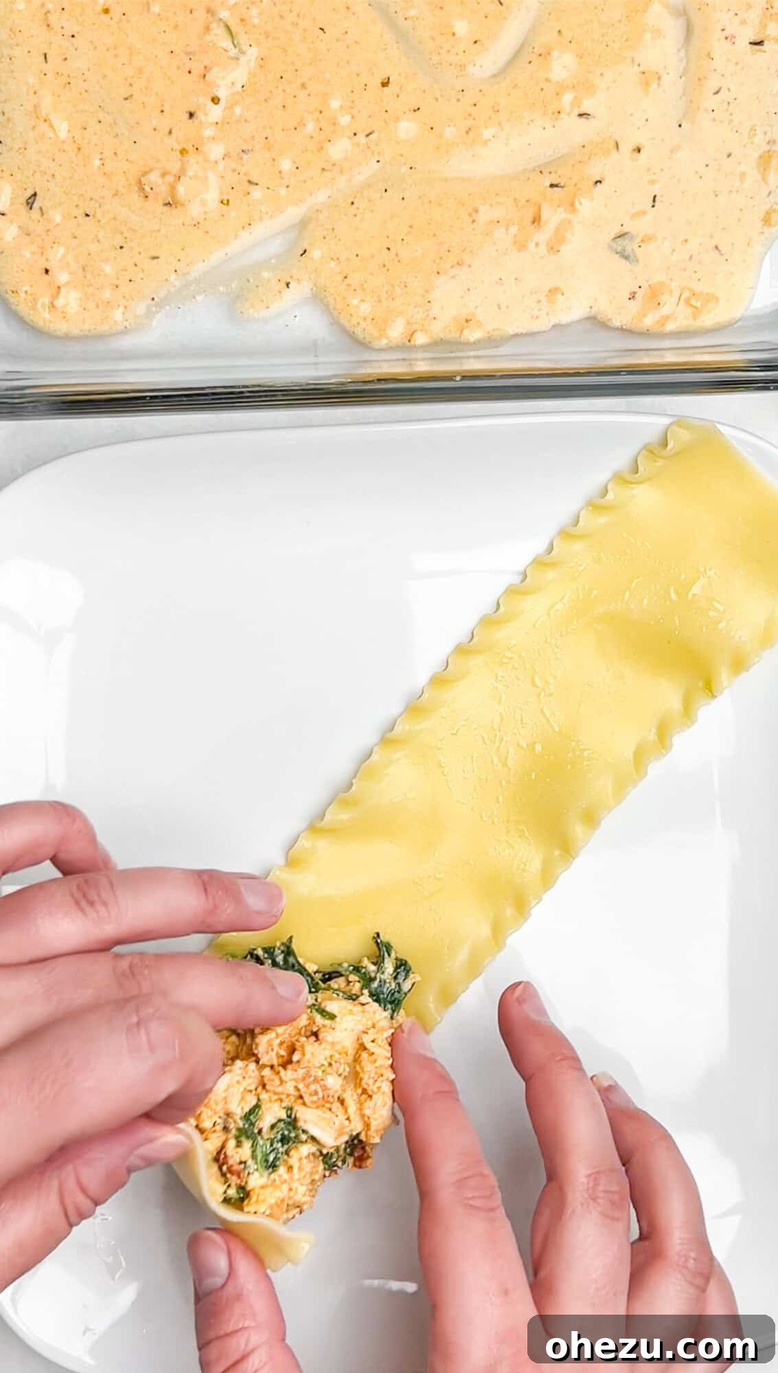 Tightly rolling a lasagna noodle filled with Cajun chicken mixture