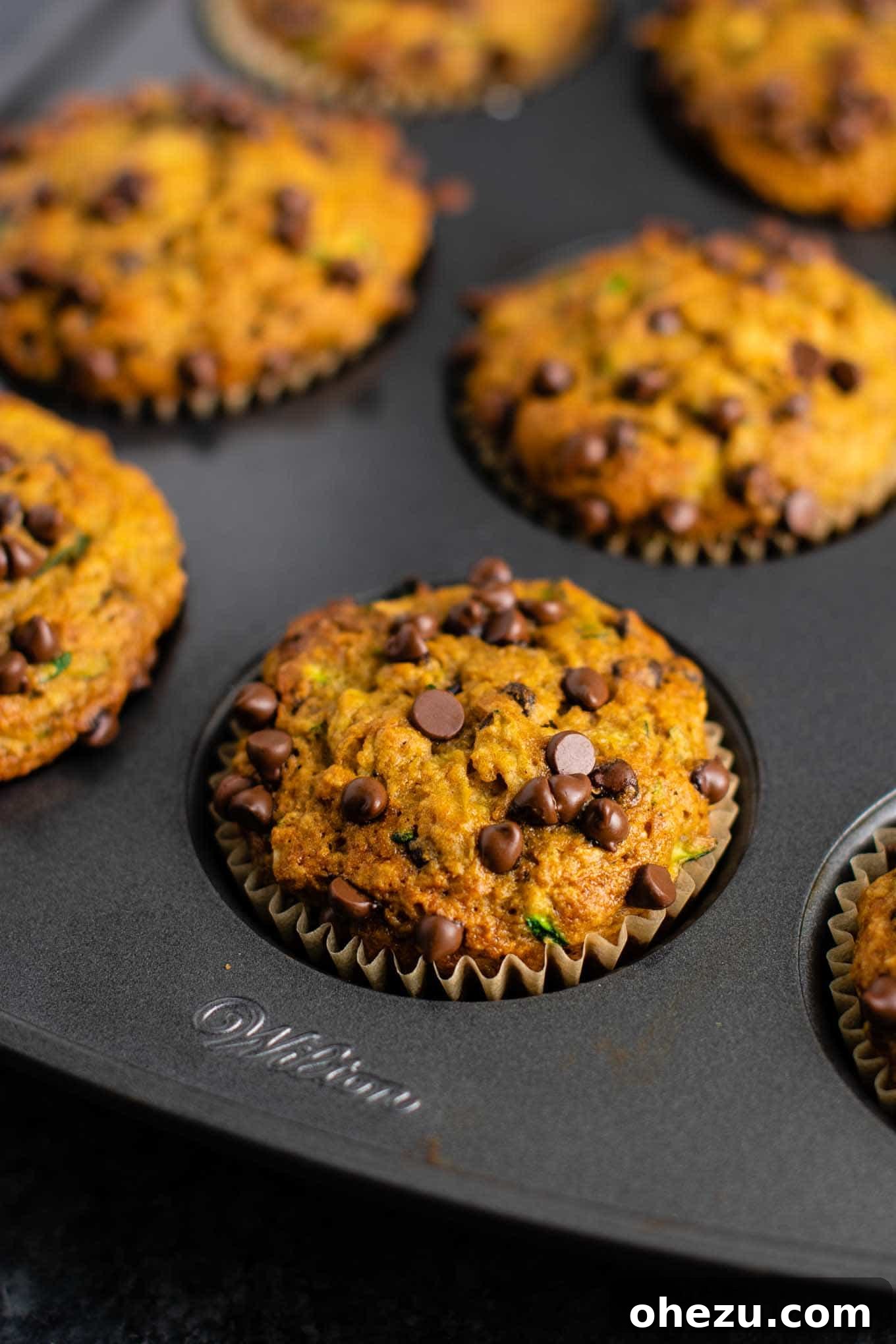 Muffin batter being gently folded with a rubber spatula in a large mixing bowl, showing the perfect consistency with grated zucchini and chocolate chips.