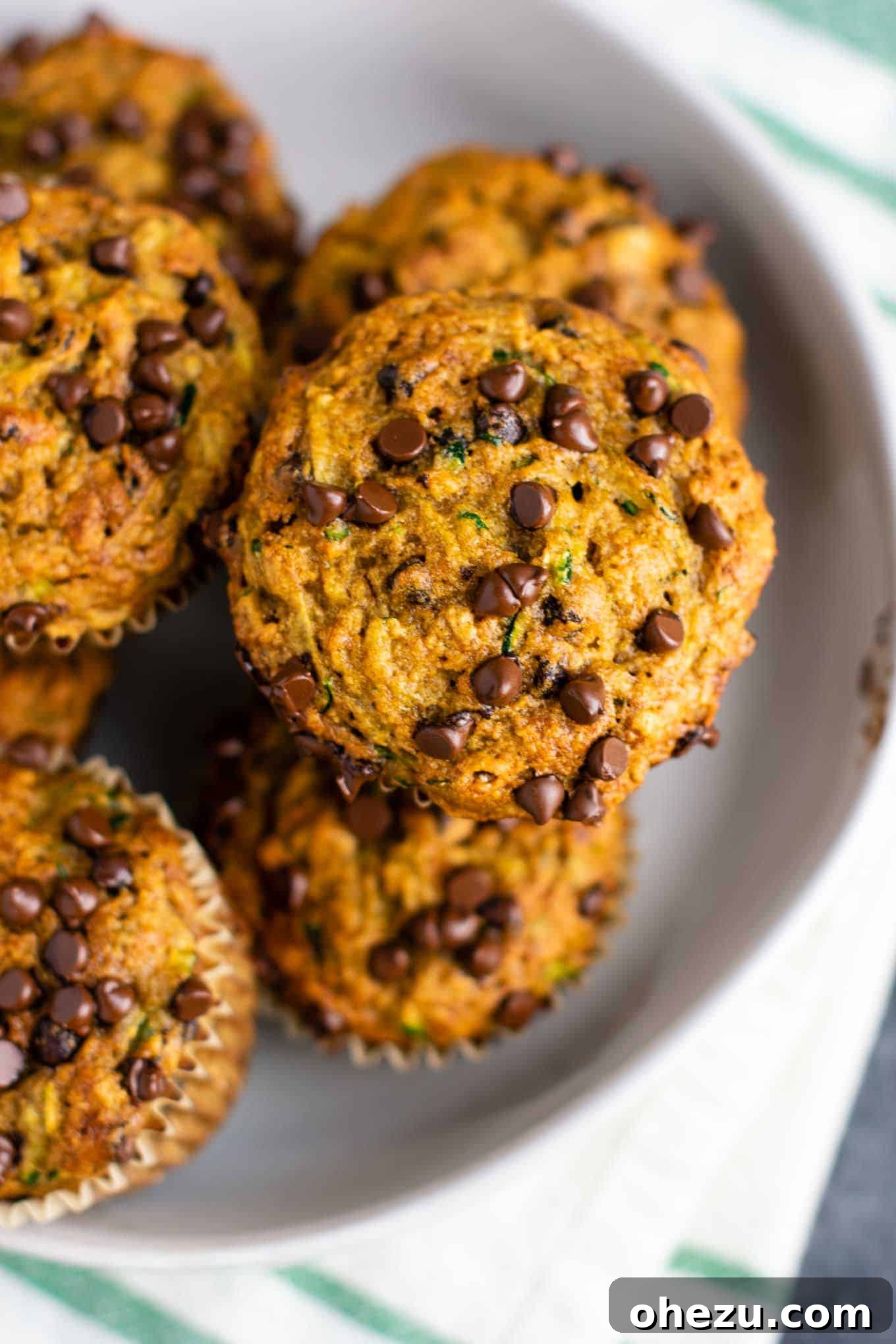 Baked zucchini chocolate chip muffins cooling in a parchment-lined muffin tin, with perfectly golden tops.