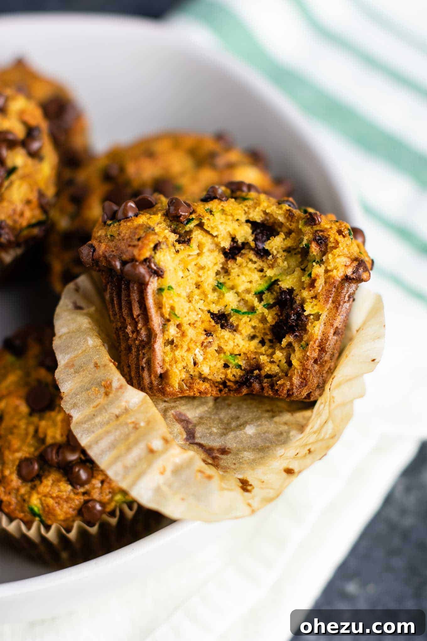 A stack of three dairy-free zucchini chocolate chip muffins on a rustic wooden board, showing their fluffy texture and abundant chocolate chips.