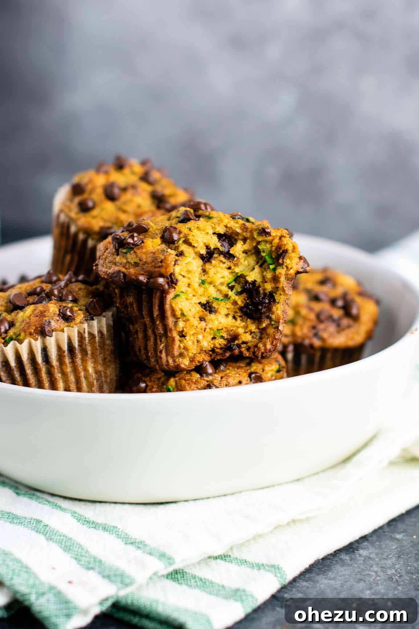 A single zucchini chocolate chip muffin torn open to reveal its moist interior, melted chocolate, and specks of green zucchini.