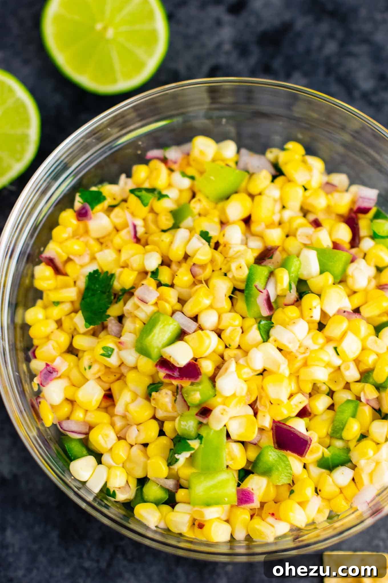 All the fresh ingredients for corn salsa in a bowl, before mixing, showing corn, red onion, bell pepper, and cilantro.