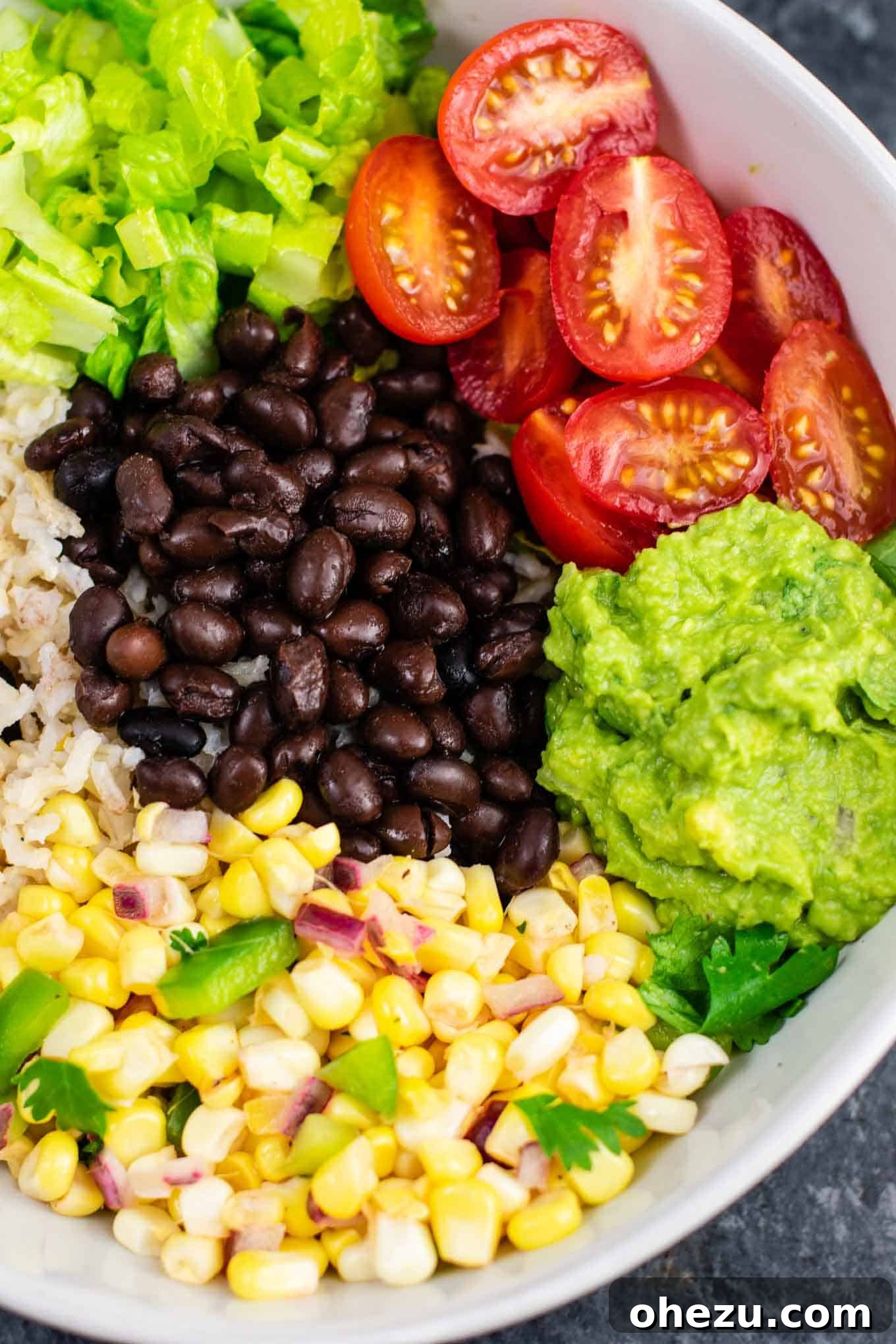 A close-up of a beautifully assembled vegan burrito bowl, showcasing layers of rice, black beans, corn salsa, guacamole, and fresh greens. Ideal for a wholesome vegan dinner. #burritobowlrecipe #veganfood #homemade #freshingredients #easyvegan