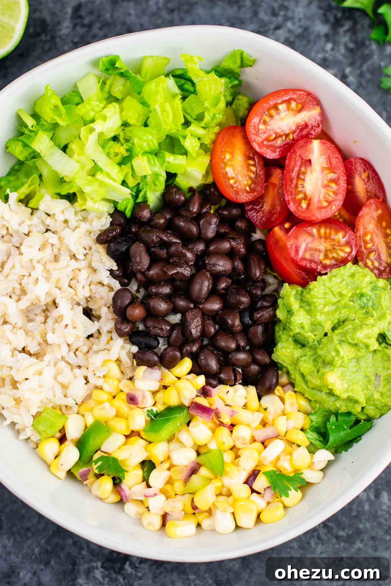 A table spread with various components of a vegan burrito bowl, including a finished bowl, a bowl of fresh guacamole, and a bowl of corn salsa. Perfect for entertaining or a family dinner. #burritobowlmeal #veganfriendly #healthydinner #homemadeisthebest