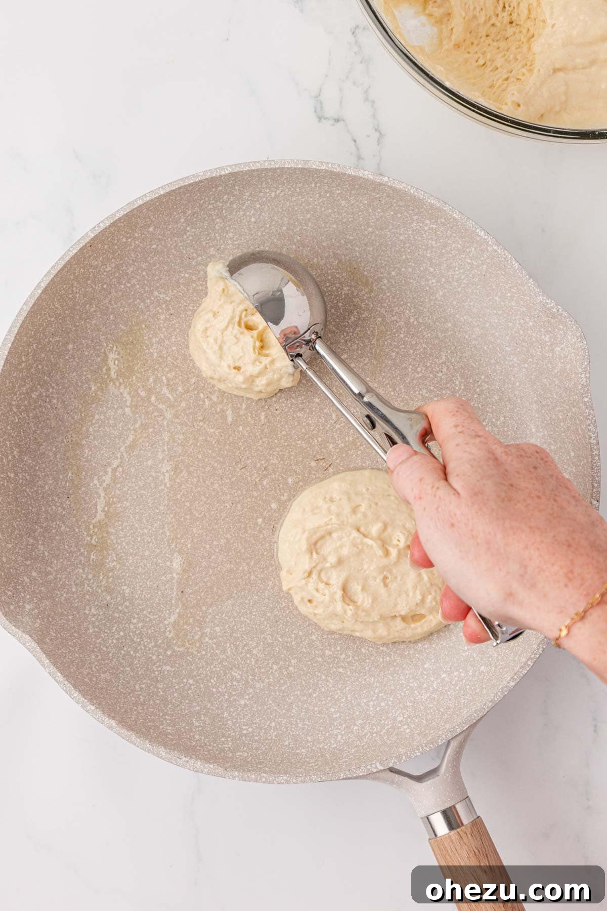 Spoonful of pancake batter being dropped onto a hot skillet.