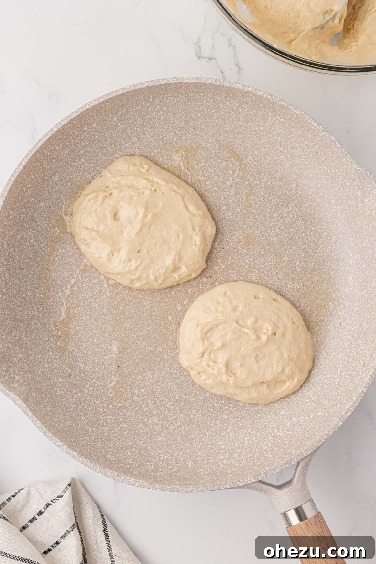 Pancake batter sizzling gently in a skillet, showing bubbles forming.