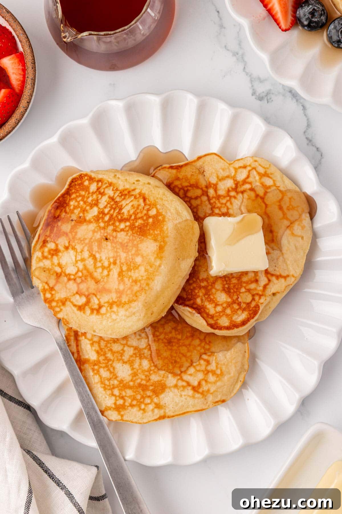 A large stack of golden-brown Greek yogurt pancakes on a white plate, ready to be topped.