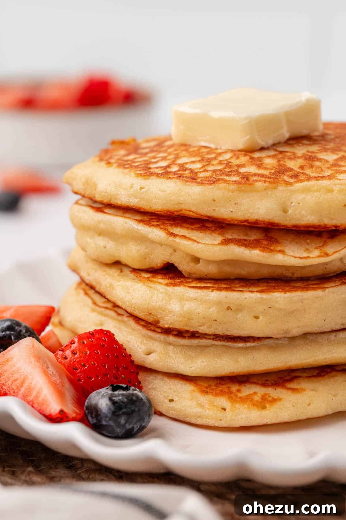 Close-up of a stack of Greek yogurt pancakes with melted butter, maple syrup, and blueberries.