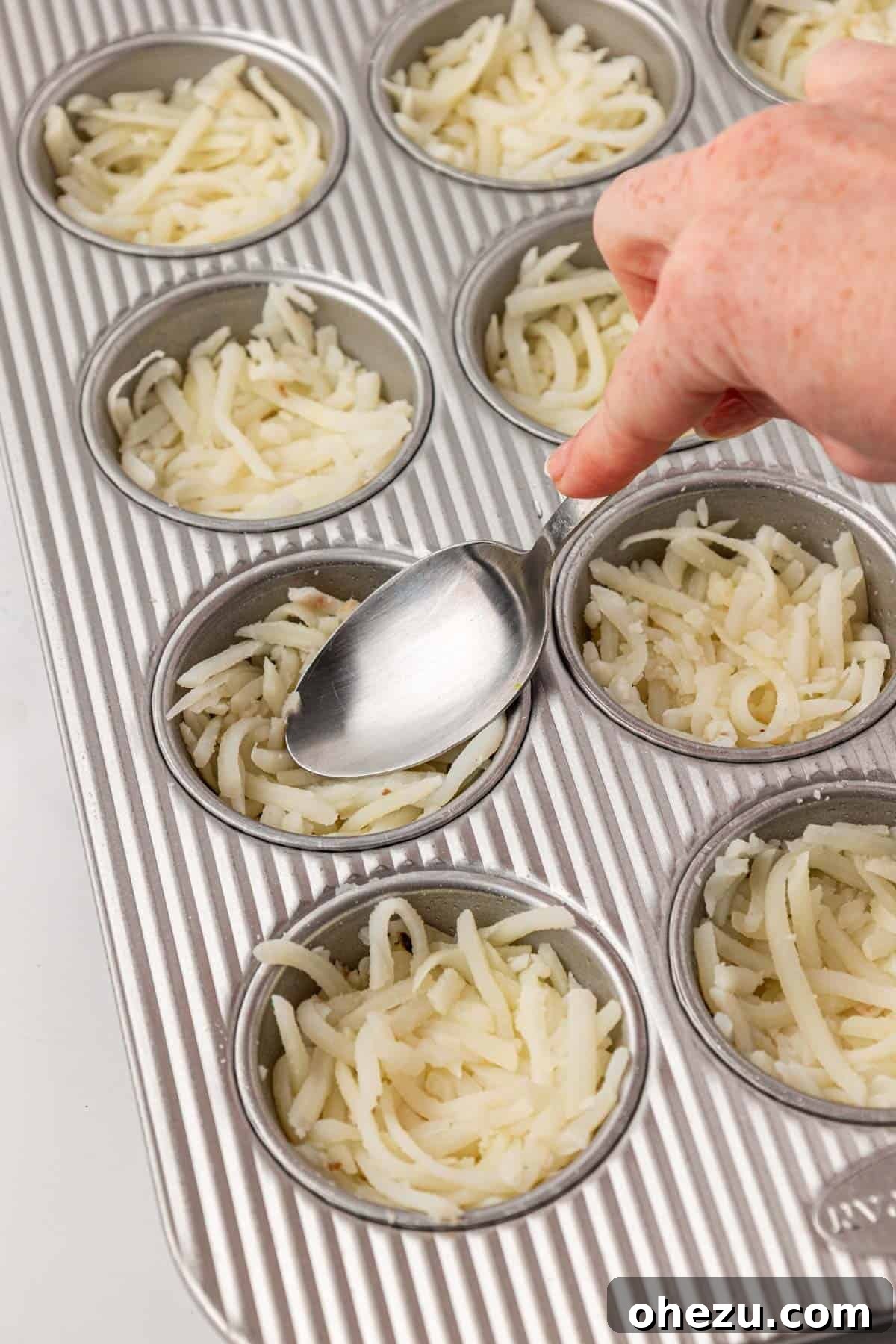 using a spoon to press hash browns into a muffin tin for even distribution