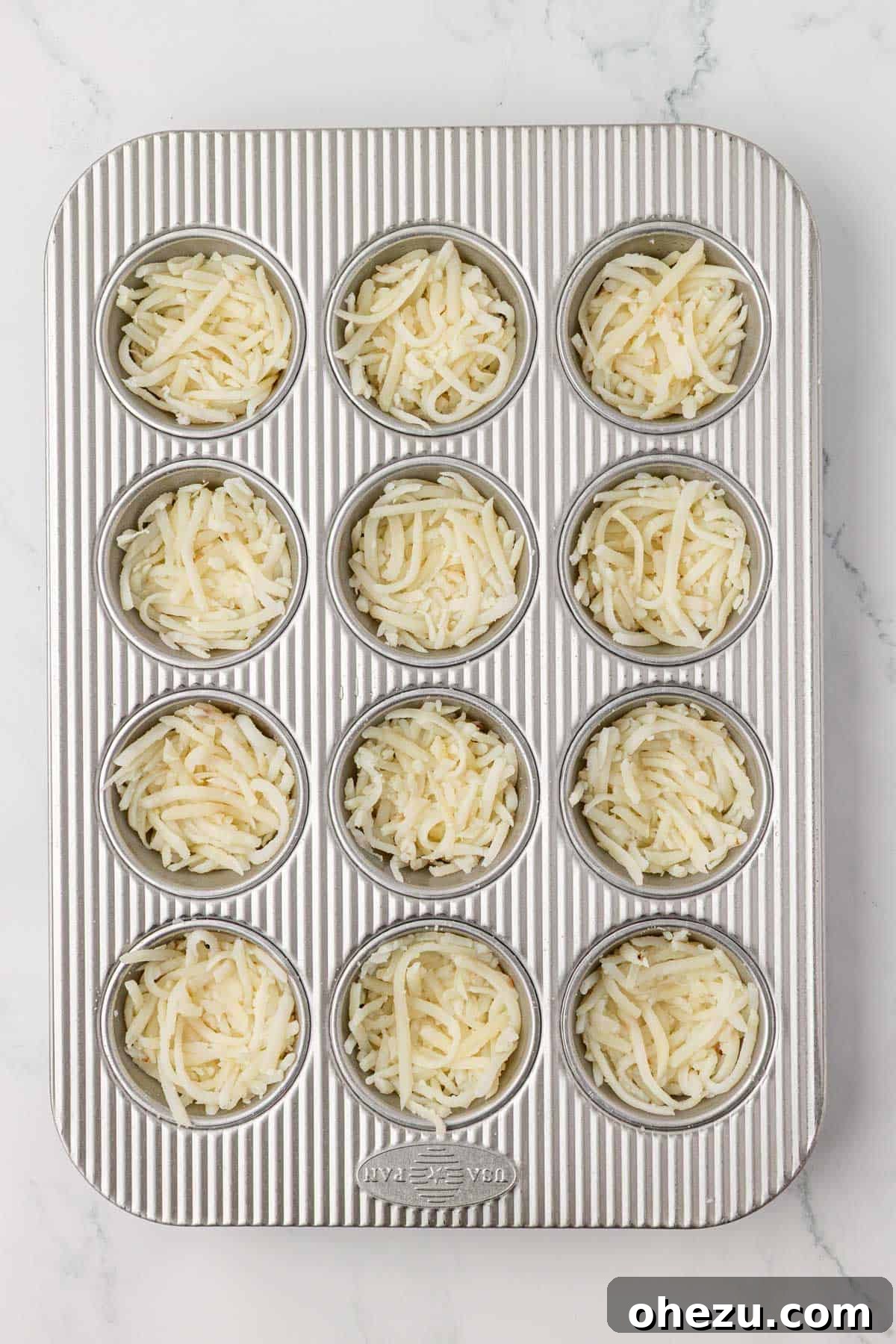 hash browns pressed down and ready for the first bake in a muffin tin