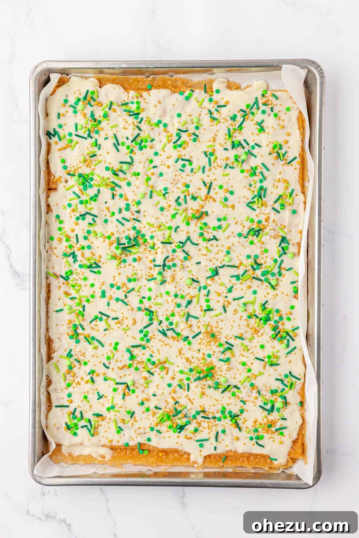 Generously adding festive St. Patrick's Day sprinkles over the melted white chocolate layer.