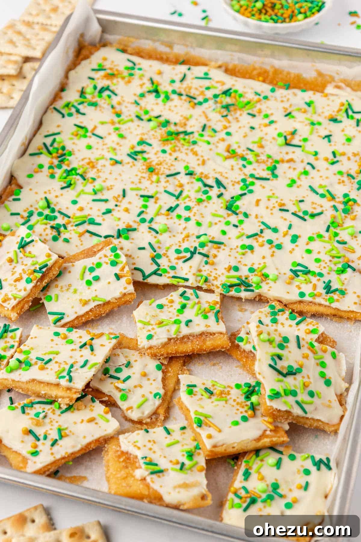 A finished slab of saltine toffee with white chocolate and green and gold sprinkles, ready to be broken into pieces.