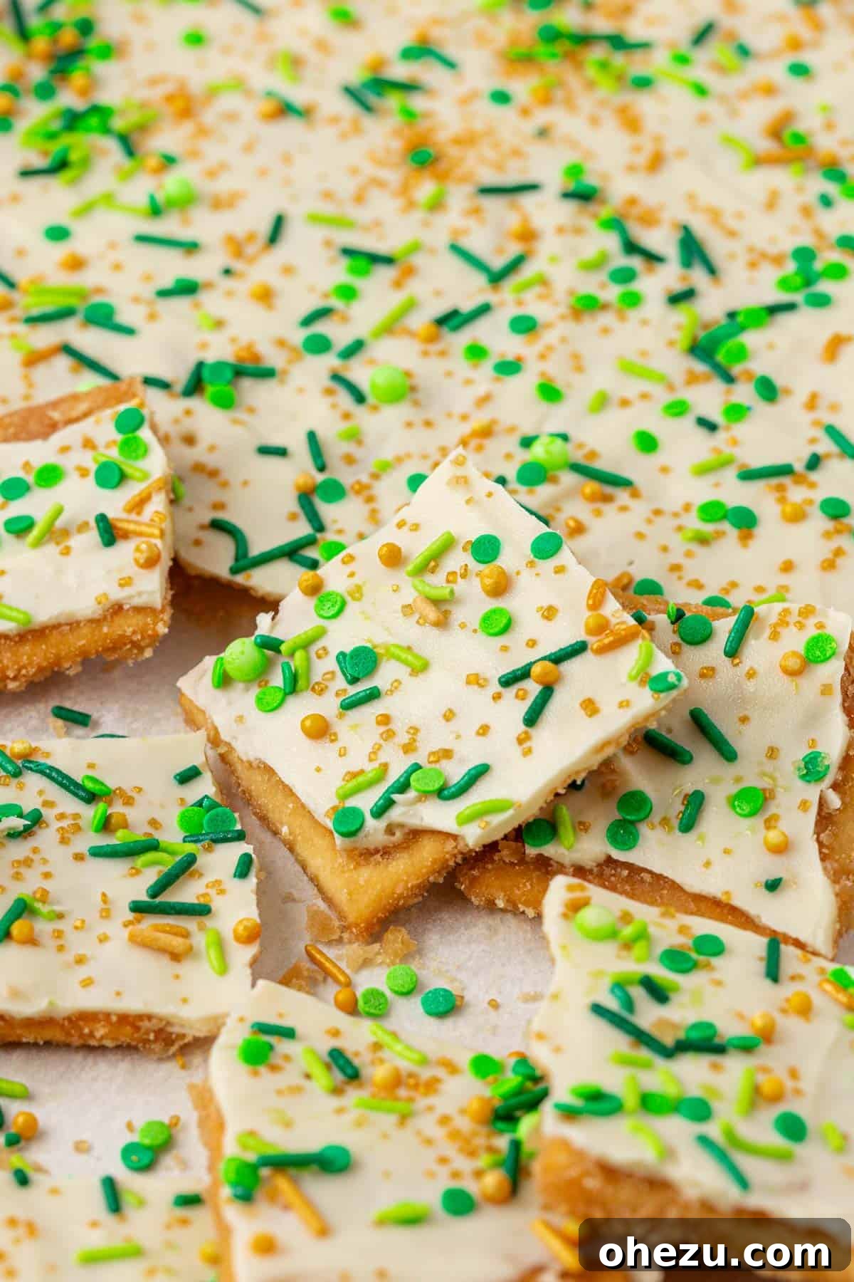 Pieces of saltine toffee with white chocolate and green and gold sprinkles arranged beautifully on a white plate.