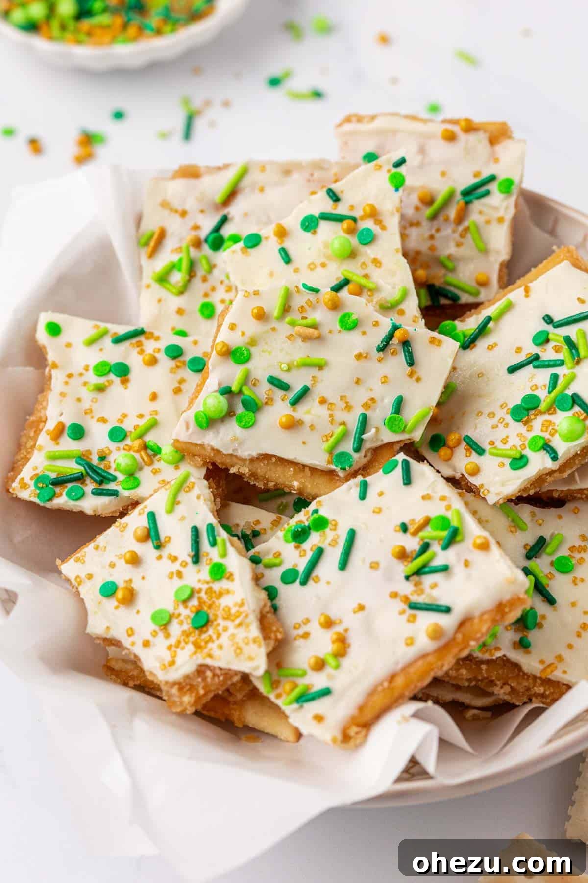 A close-up of several individual pieces of Leprechaun Crack on a rustic surface, showcasing the layers of cracker, toffee, white chocolate, and sprinkles.