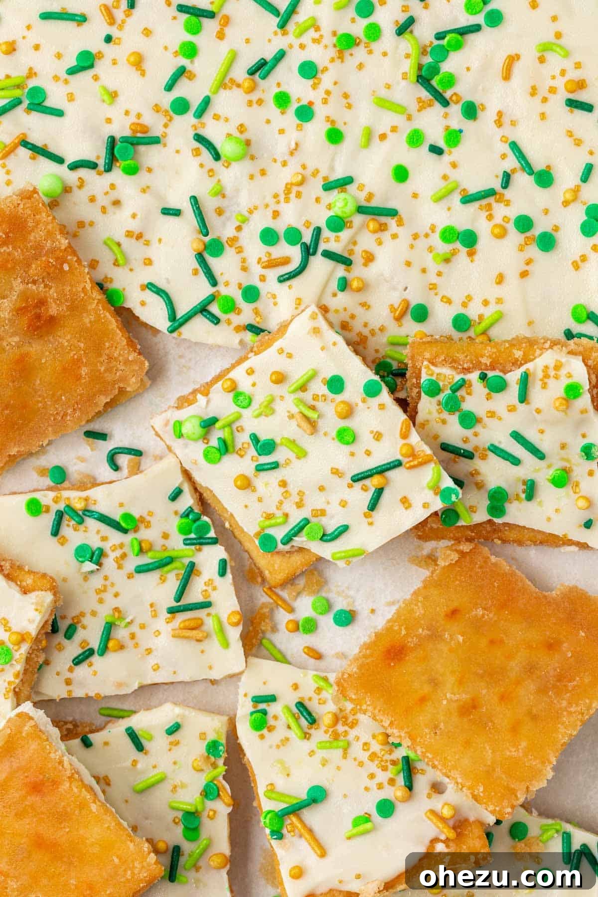 A large batch of St. Patrick's Day saltine toffee with white chocolate and green sprinkles, broken into various pieces.