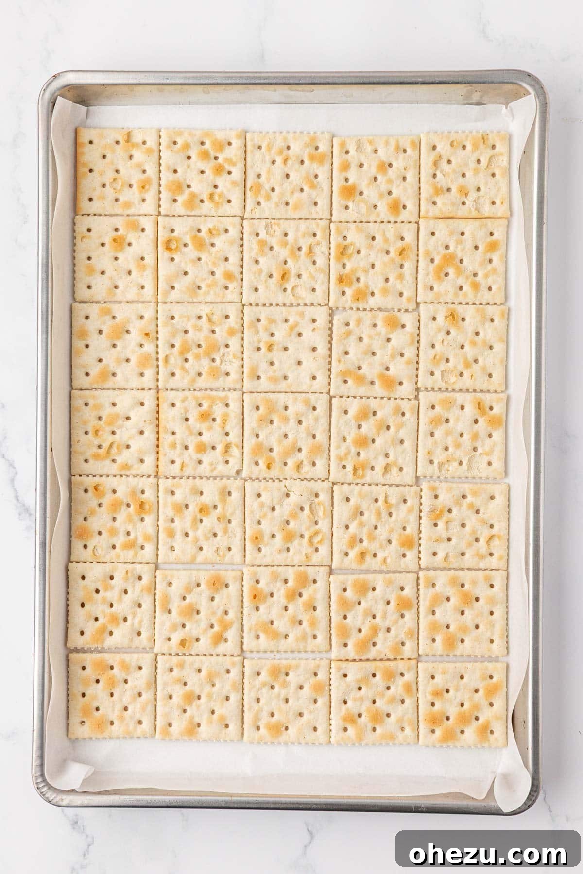 Saltine crackers carefully lined up in rows on a baking sheet covered with parchment paper.