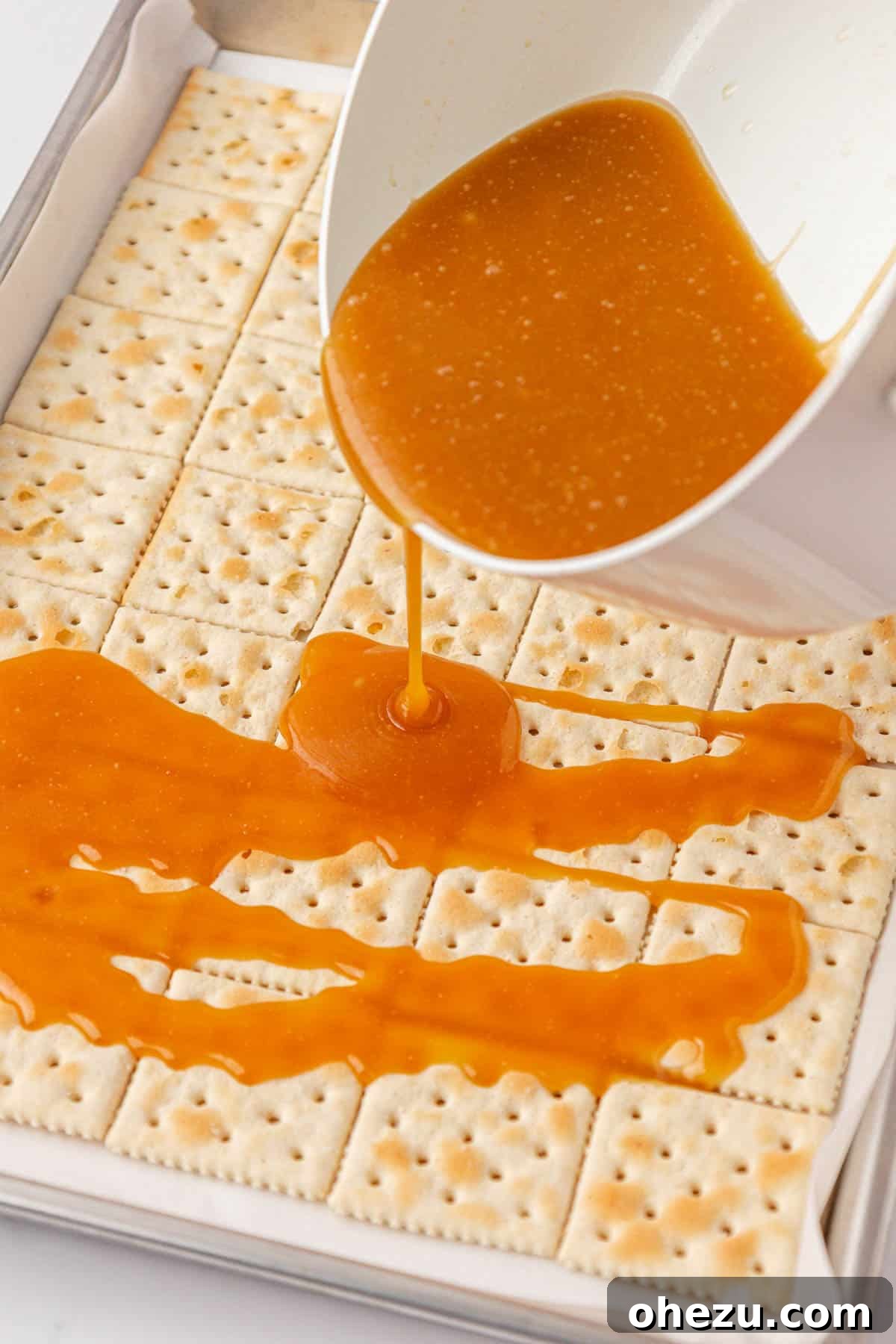 Pouring the hot, shimmering toffee mixture over the saltine crackers on the baking sheet.