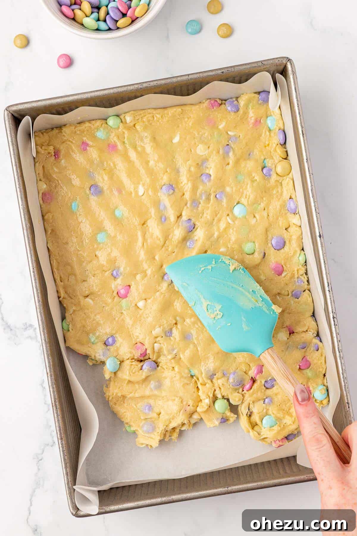 Pressing the cookie batter into a baking dish with a rubber spatula.