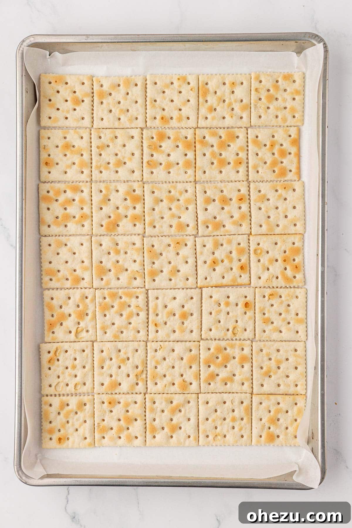 A baking sheet meticulously lined with saltine crackers, prepared to receive the toffee mixture