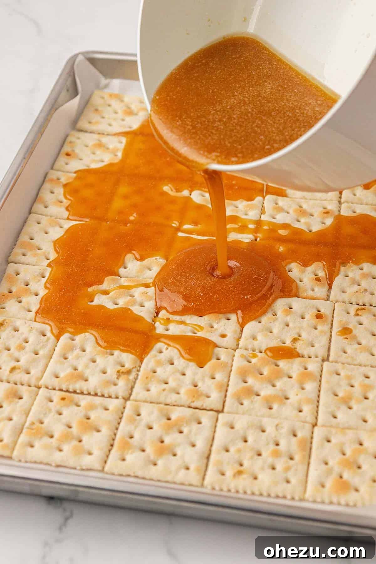 Carefully pouring the hot, melted toffee evenly over the saltine crackers on a baking sheet