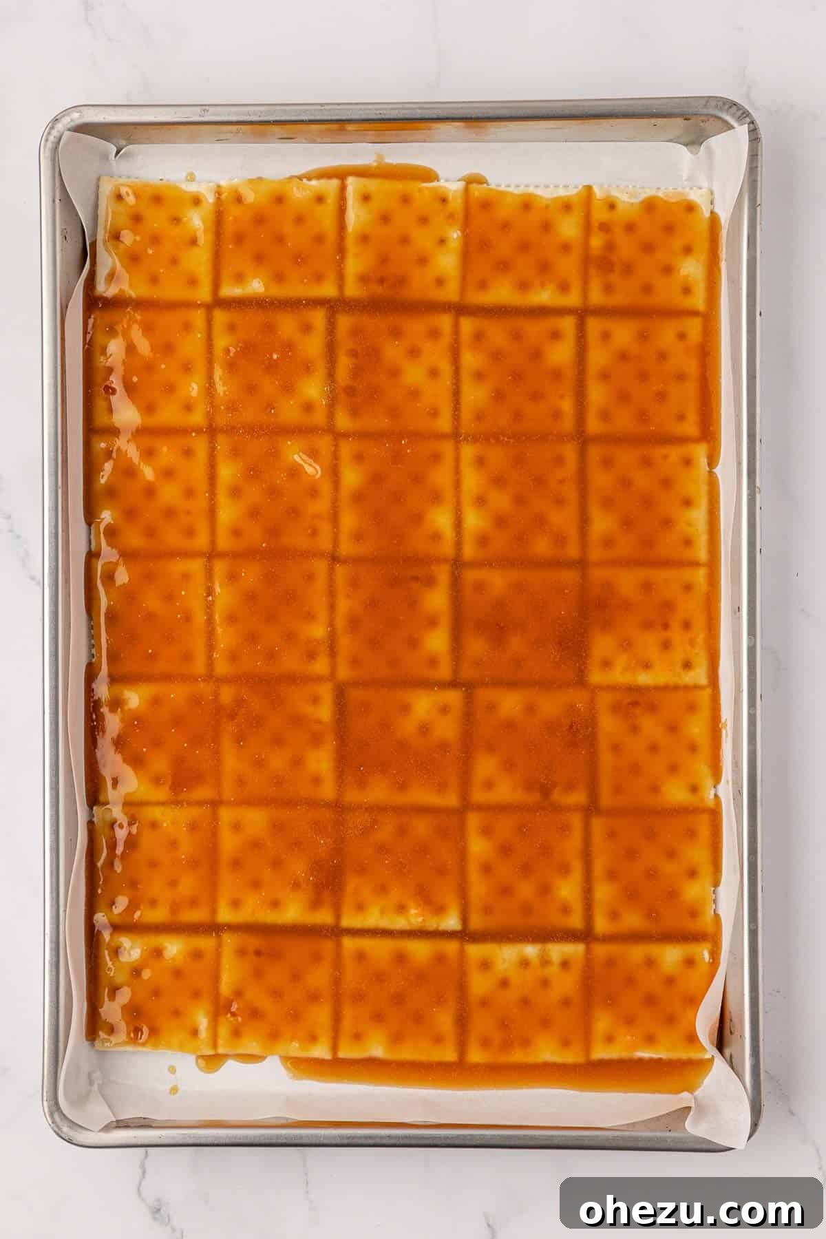 Saltine crackers uniformly coated with the toffee mixture, awaiting baking